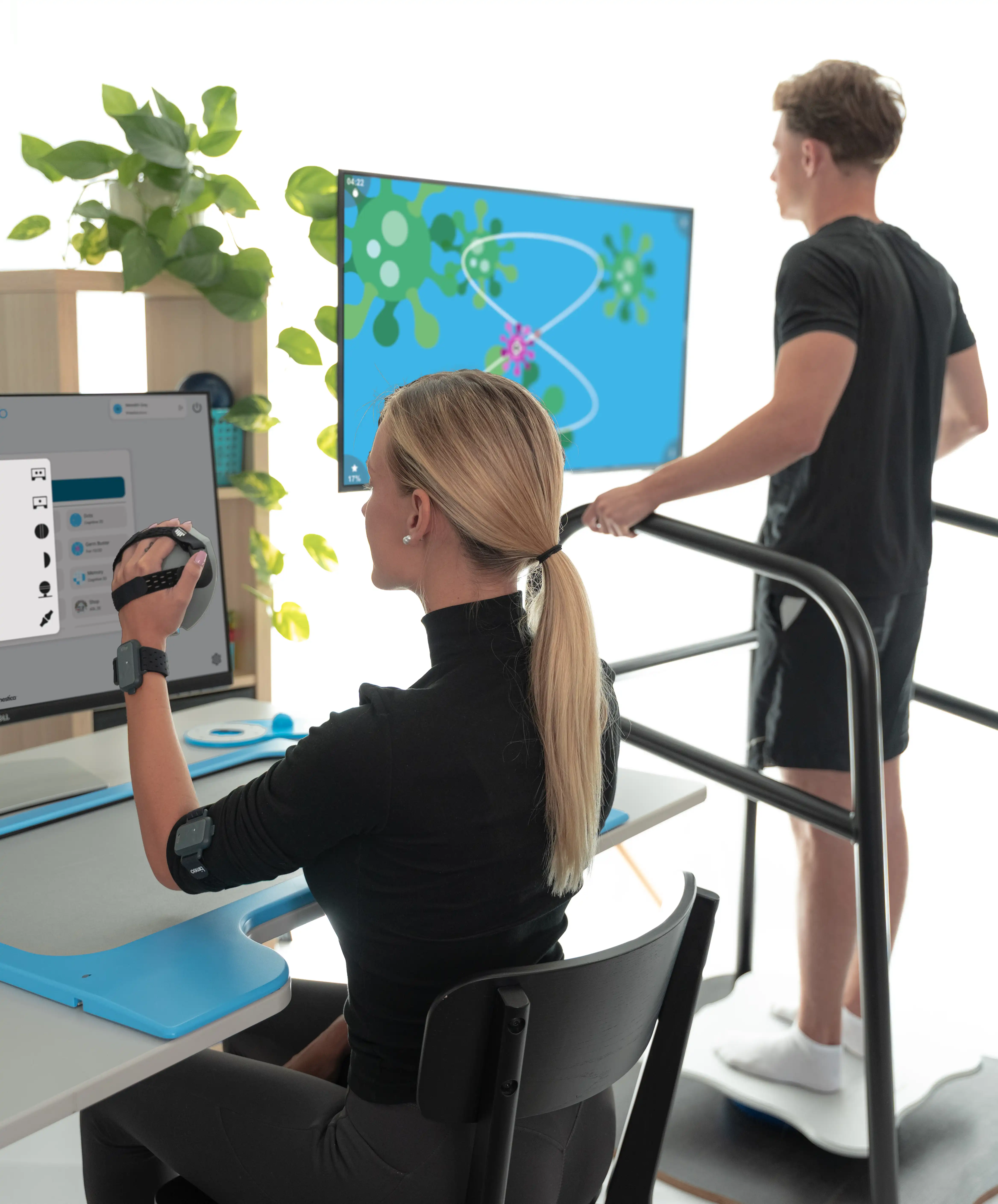 A clinic scene with a patient using Bimeo arm rehabilitation device and another patient on Equio balance system.